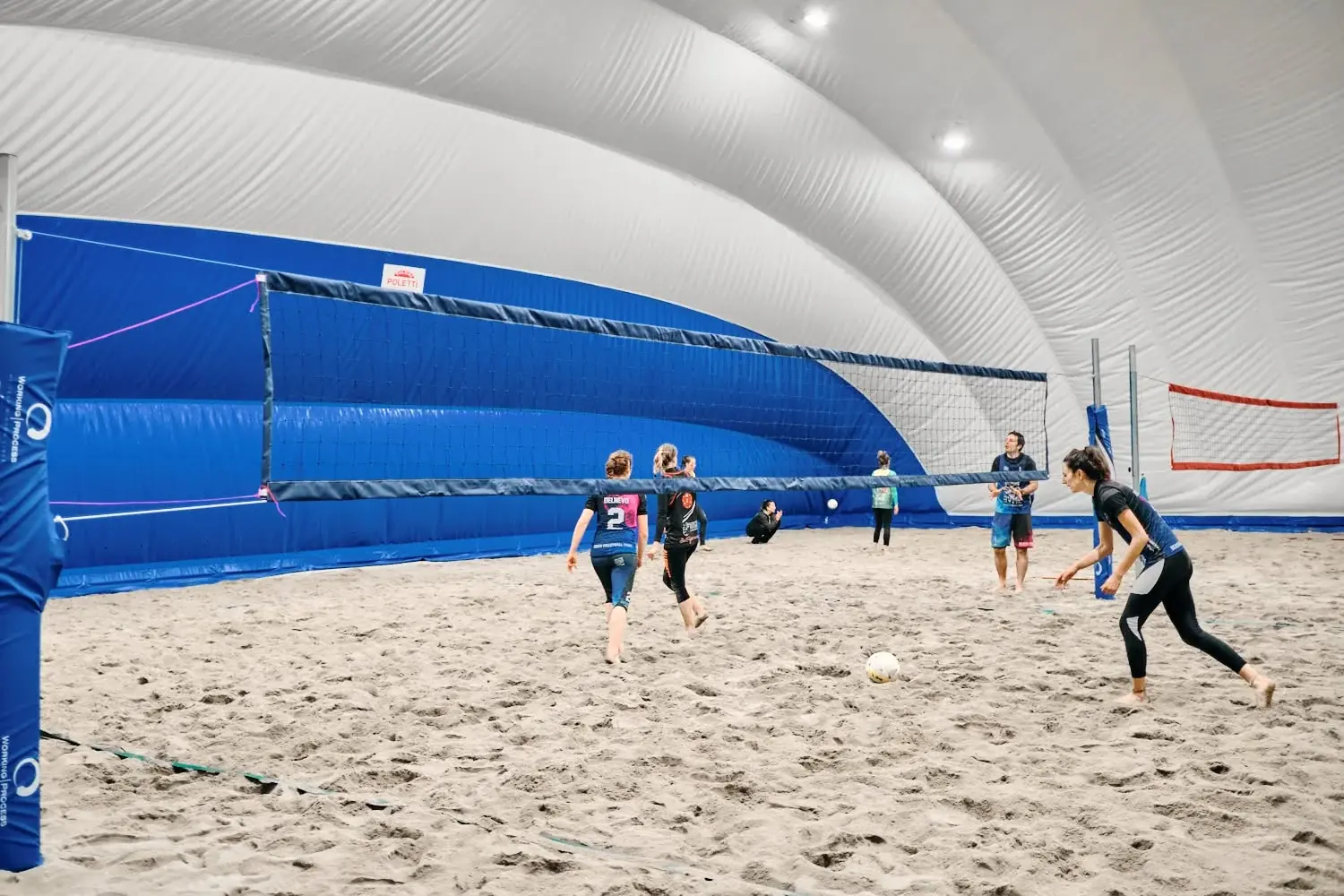 Atlete giocano a beach volley su un campo di sabbia al coperto. Archivio BVME 2022.